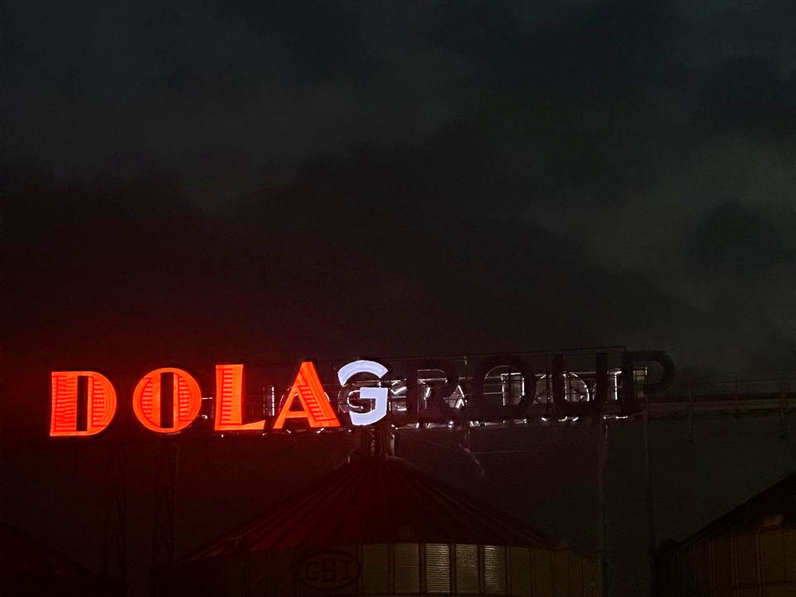 Red illuminated Dola Group rooftop sign glowing at dusk